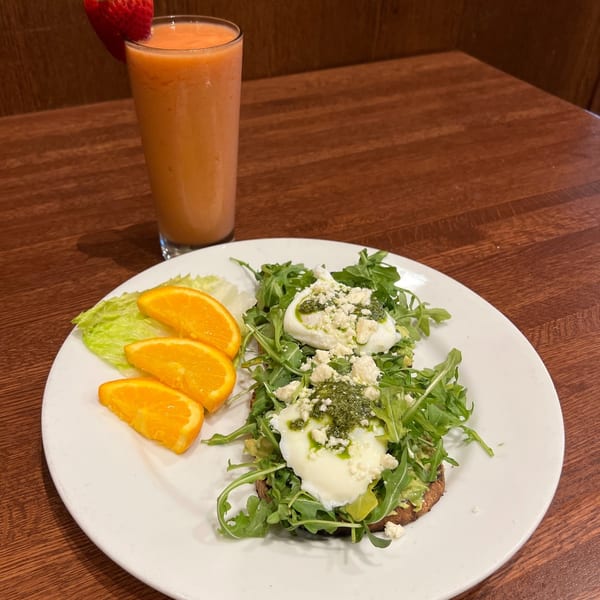 Avocado toast with poached eggs, pesto, feta, arugula, orange slices, and a strawberry smoothie.