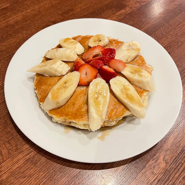 Fluffy pancakes topped with sliced bananas, strawberries, and a drizzle of syrup on a white plate.