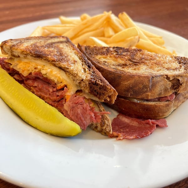 A grilled Reuben sandwich with corned beef, sauerkraut, and cheese, served with fries and a pickle spear.