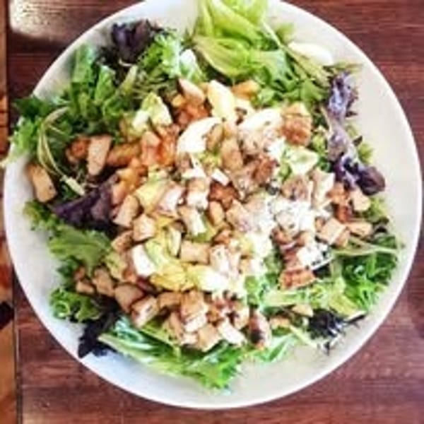 Overhead view of a vibrant mixed greens salad with diced chicken and avocado in a white bowl.