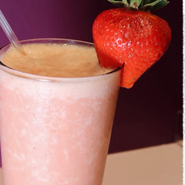 Strawberry smoothie in a glass with a fresh strawberry garnish and a straw.