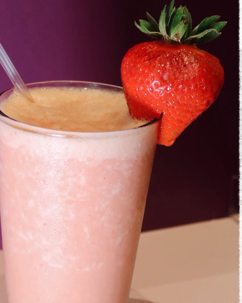 Strawberry smoothie in a glass with a fresh strawberry garnish and a straw.