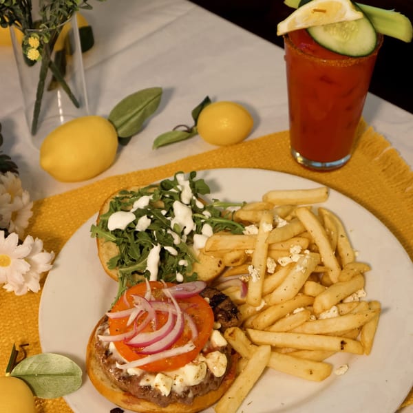 A burger with feta, tomato, and red onion, served with fries and a Bloody Mary.